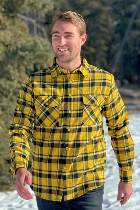 A man wearing a long-sleeved yellow and black flannel plaid shirt with two flap breast pockets and a button cuff.
