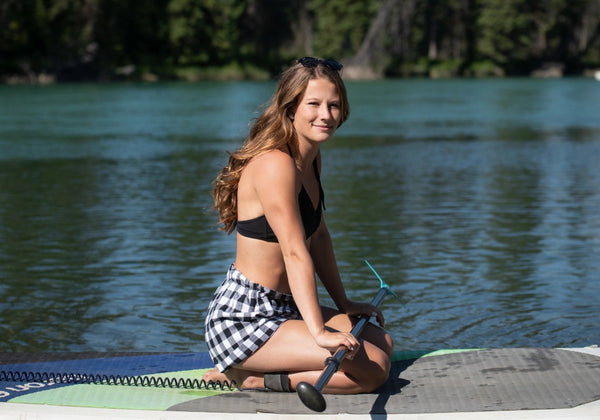 GIrl in flannel shorts laying down on an SUP board