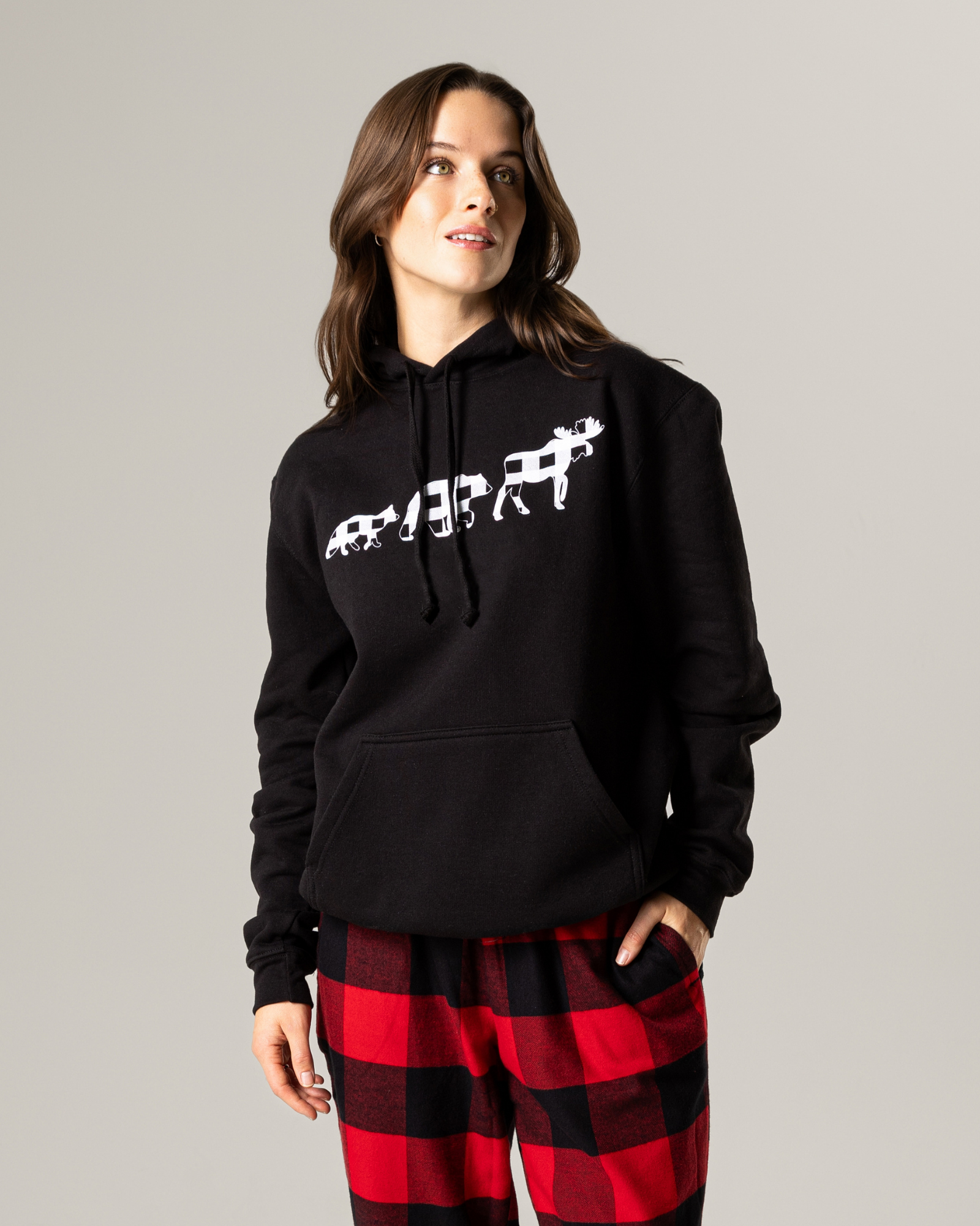 Person wearing a black hoodie with a white graphic and red plaid pants on a gray background