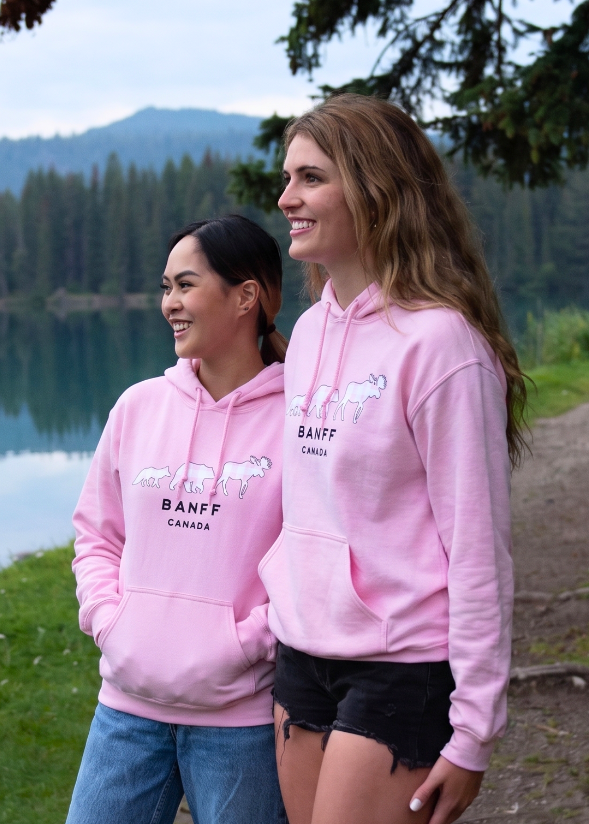 Two women wearing pink hoodies with Banff branding by a lake.