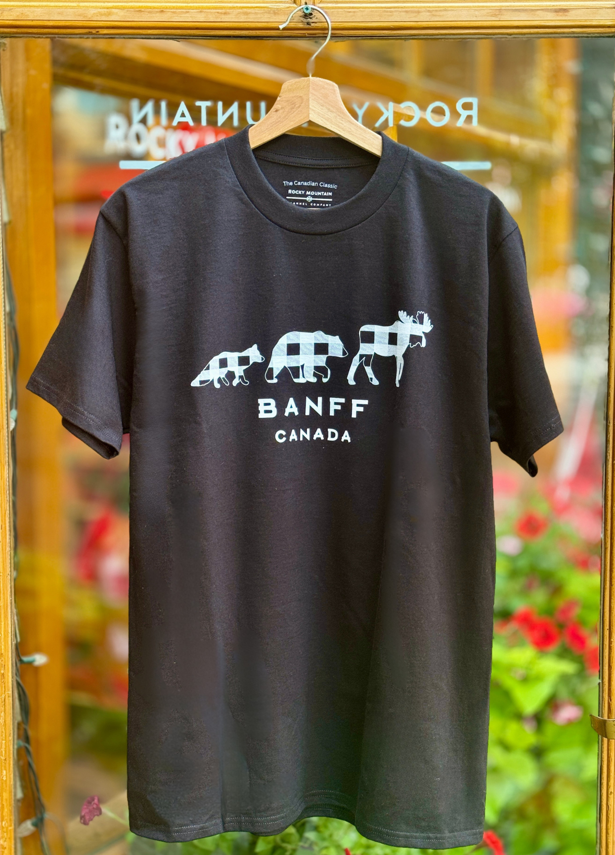 Black t-shirt with white text and graphics on a hanger against a blurred background