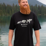 Man wearing a black t-shirt with 'Banff Canada' design standing by a lake with mountains in the background.