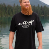 Man wearing a black t-shirt with 'Banff Canada' design standing by a lake with mountains in the background.