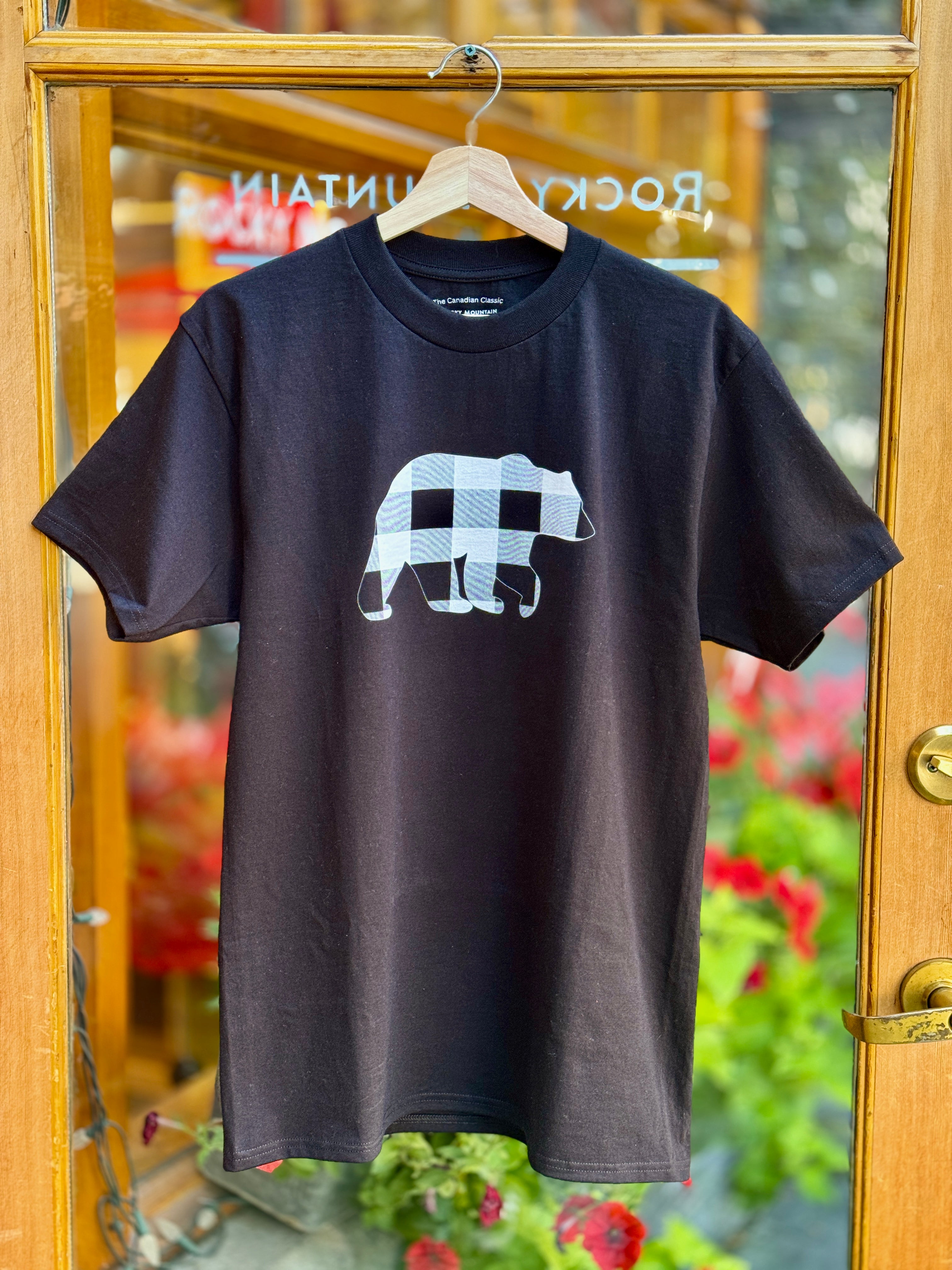 Black t-shirt with a white bear graphic on a hanger in front of a glass door.