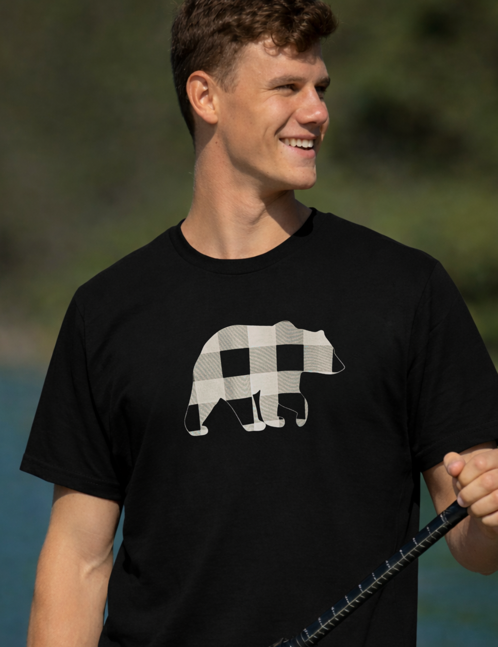 Man wearing a black t-shirt with a bear graphic, holding a fishing rod outdoors.