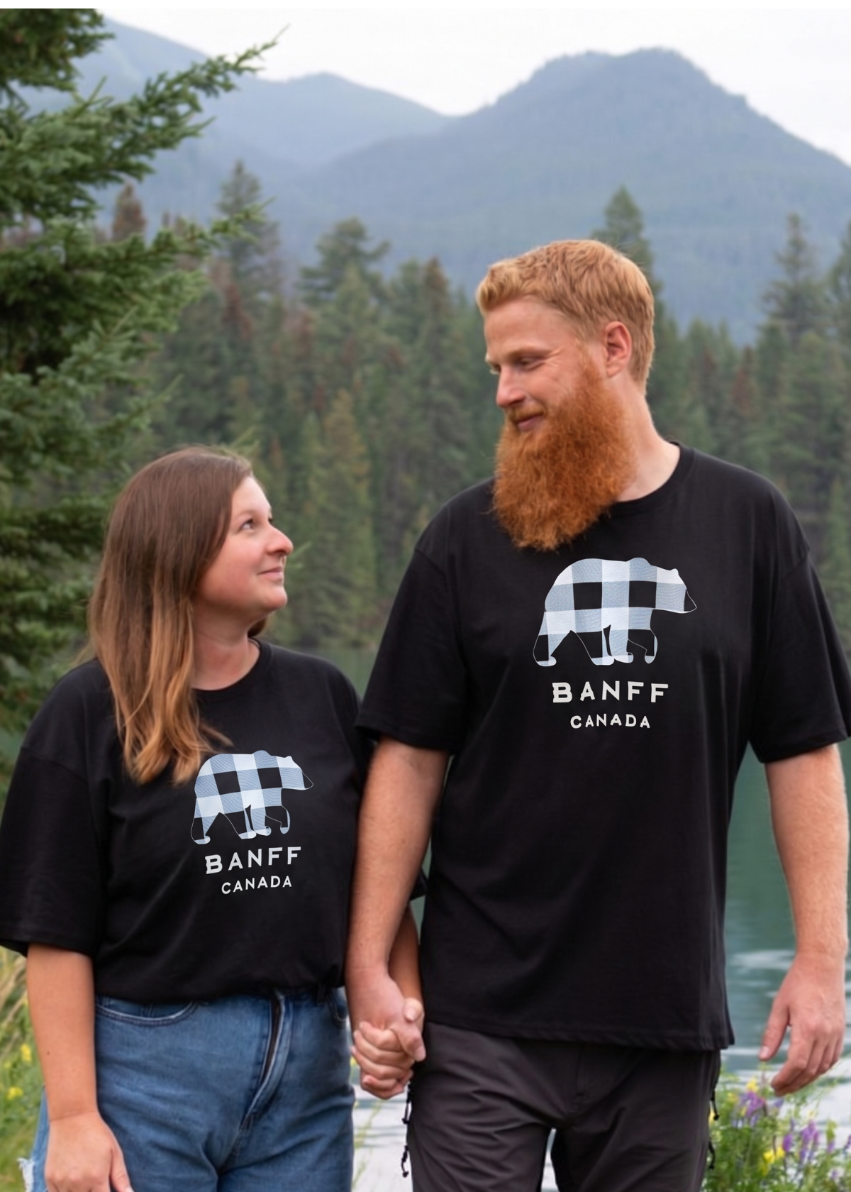Two people wearing black Banff t-shirts standing in a forested area with mountains in the background.