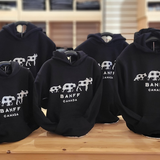 Black kids hoodies with 'Banff Canada' print on a wooden table.