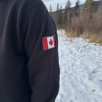 Close up of canada flag logo on left arm or a black quarter zip polo jacket.