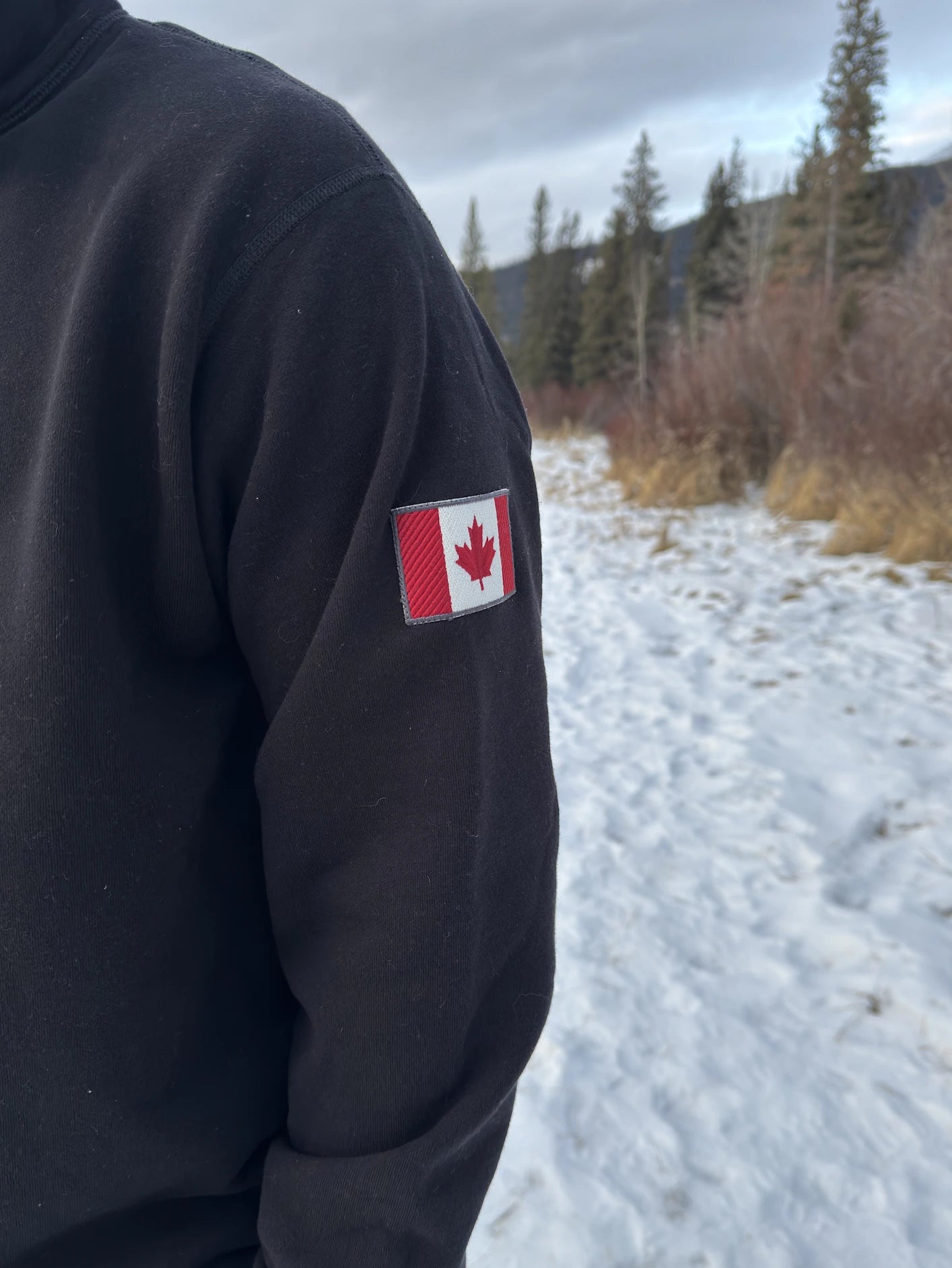 Close up of canada flag logo on left arm or a black quarter zip polo jacket.