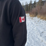 Close up of canada flag logo on left arm or a black quarter zip polo jacket.