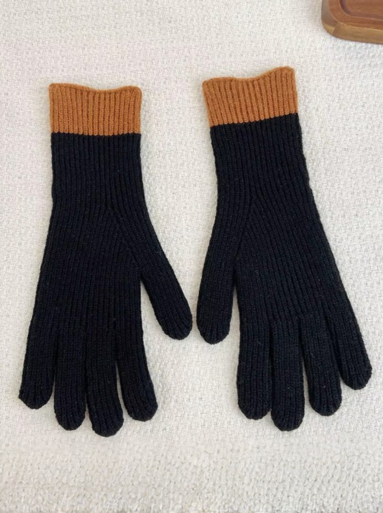 Pair of black gloves with brown cuffs on a textured white surface