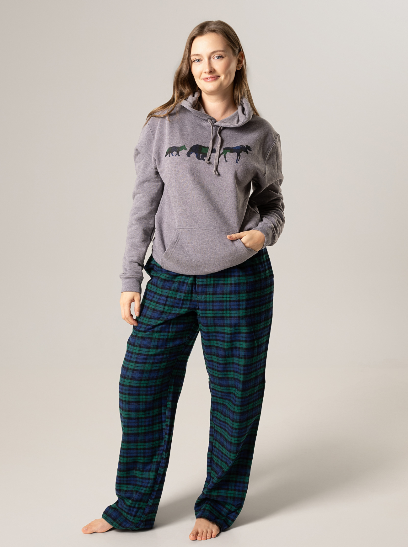 Woman wearing a gray hoodie with a graphic design and plaid pants on a plain background