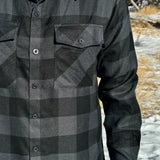 Close up of man wearing a long-sleeved black and grey buffalo check flannel shirt with two breast pockets and a button cuff.