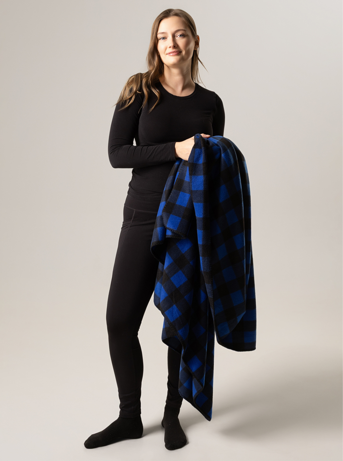 Woman holding a blue and black buffalo check blanket against a plain background