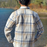 Person wearing a plaid flannel shirt by a river with mountains in the background in Banff National Park