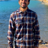 Man wearing a plaid flannel shirt standing by a river with trees in the background in Banff National Park