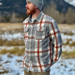 Man wearing a plaid shirt and beanie standing in a snowy landscape with mountains in the background