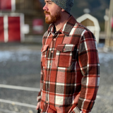 Man wearing a plaid shirt and beanie outdoors with mountains in the background