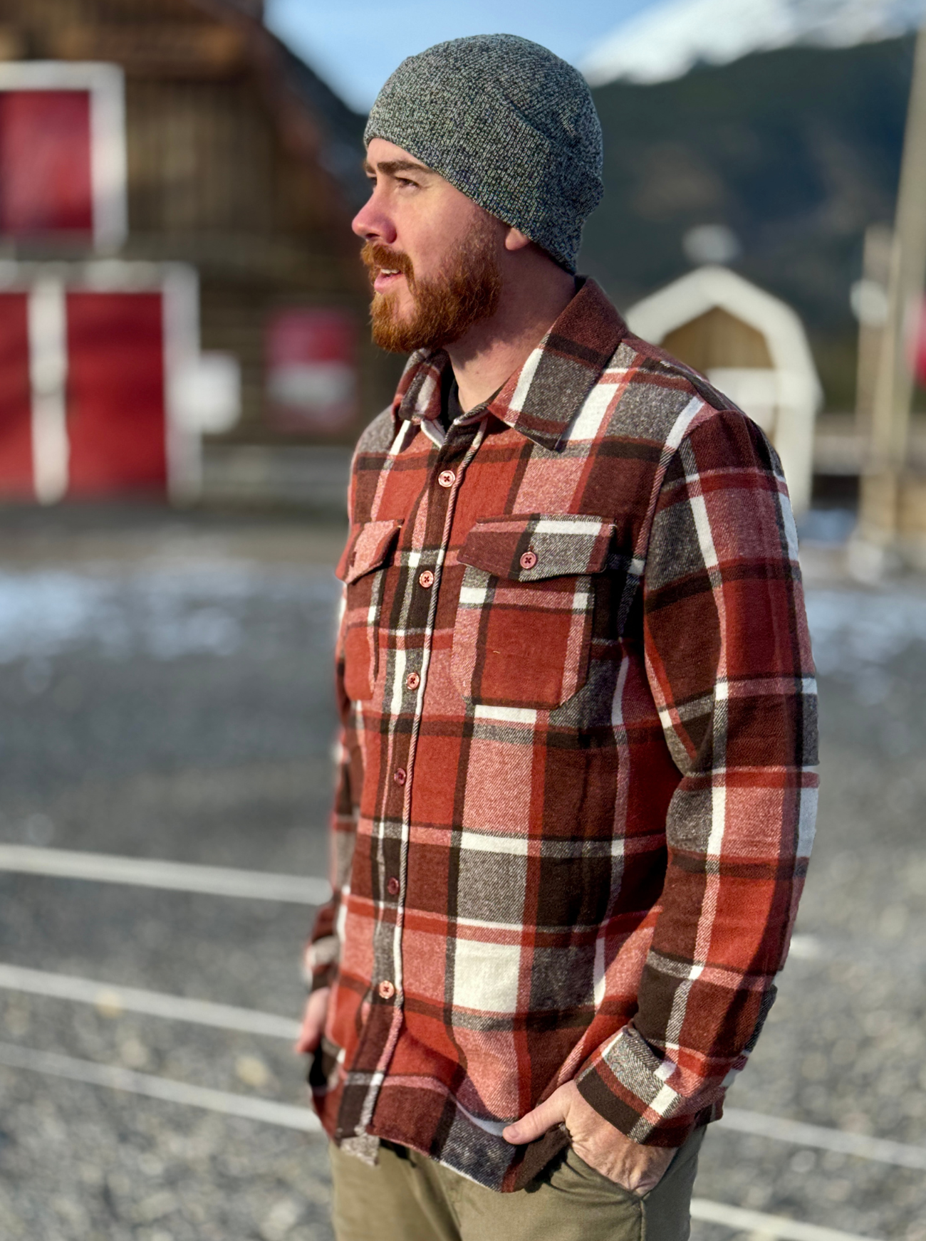Man wearing a plaid shirt and beanie outdoors with mountains in the background