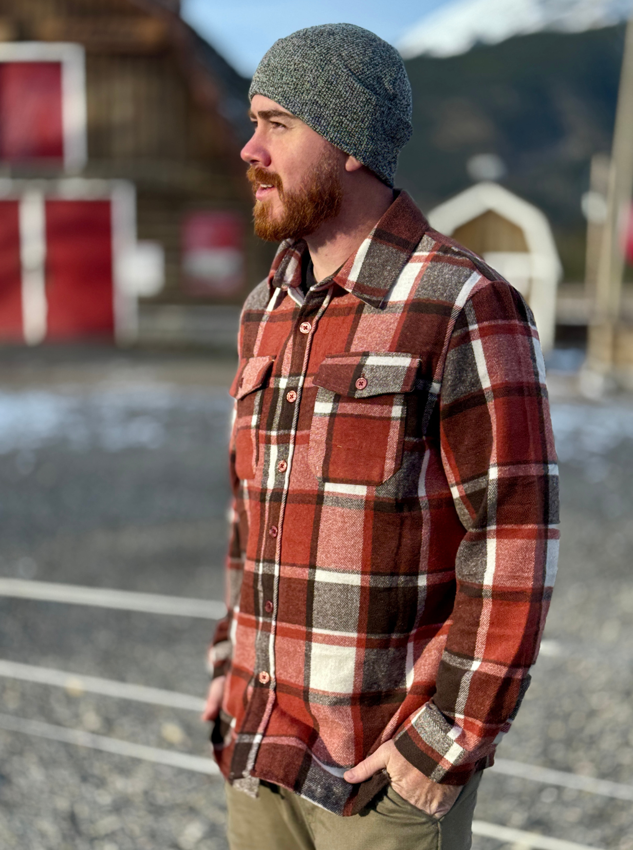 Man wearing a plaid shirt and beanie outdoors with mountains in the background