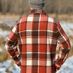 Person wearing a red and brown plaid jacket and gray beanie standing in a snowy landscape.