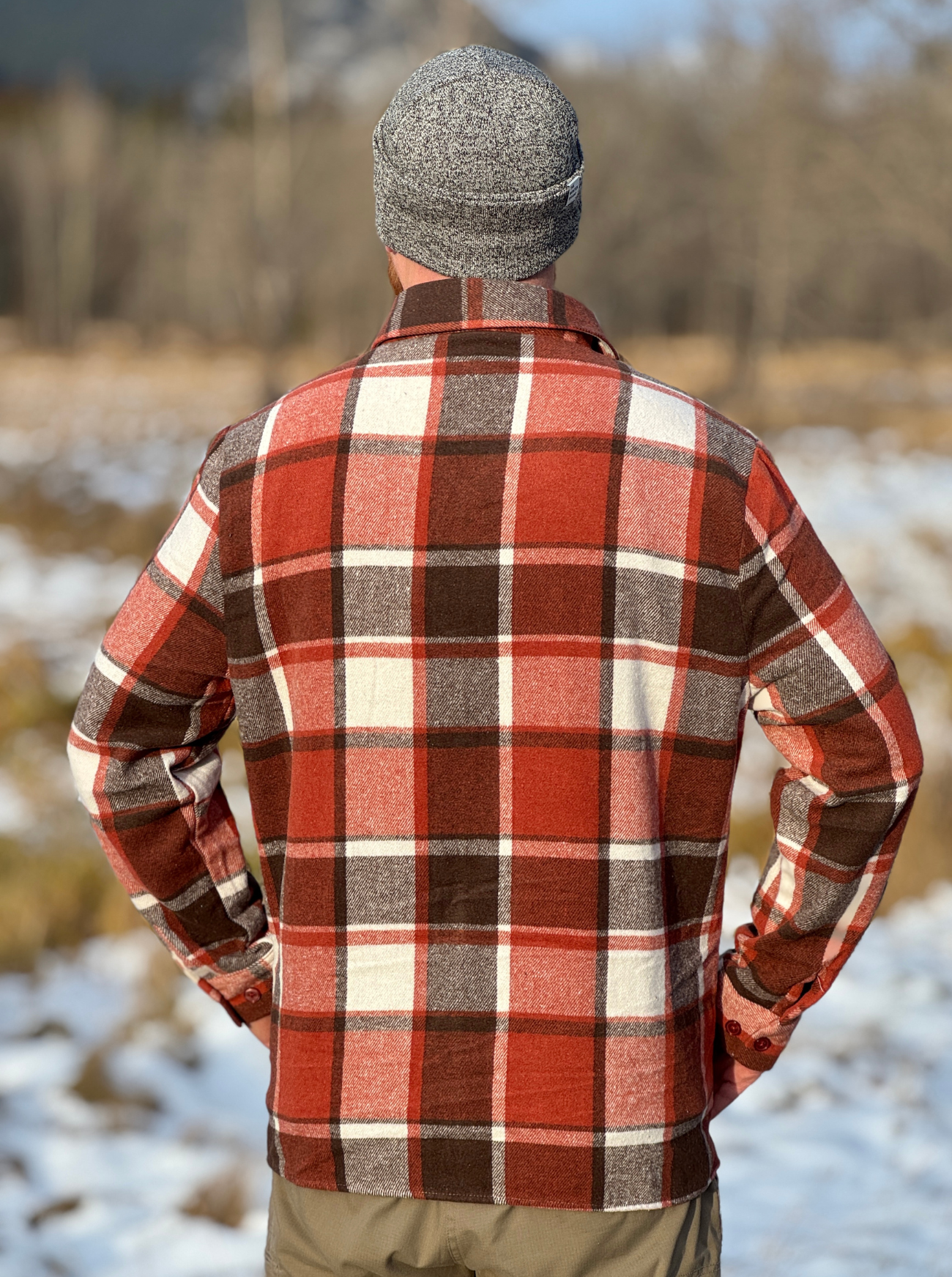 Person wearing a red and brown plaid jacket and gray beanie standing in a snowy landscape.