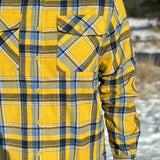 A man wearing a yellow and blue large plaid long-sleeved shirt standing outdoors.