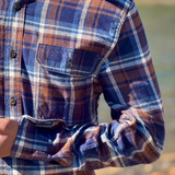 Close-up of a person wearing a plaid flannel shirt with a blurred natural background