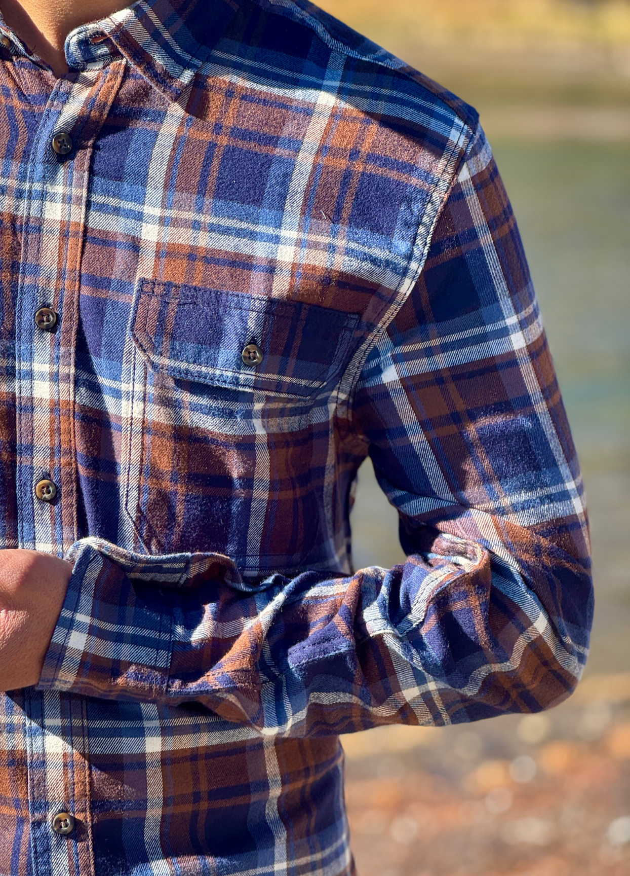 Close-up of a person wearing a plaid flannel shirt with a blurred natural background