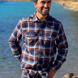 Man wearing a plaid flannel shirt standing by a river with trees in the background in Banff National Park