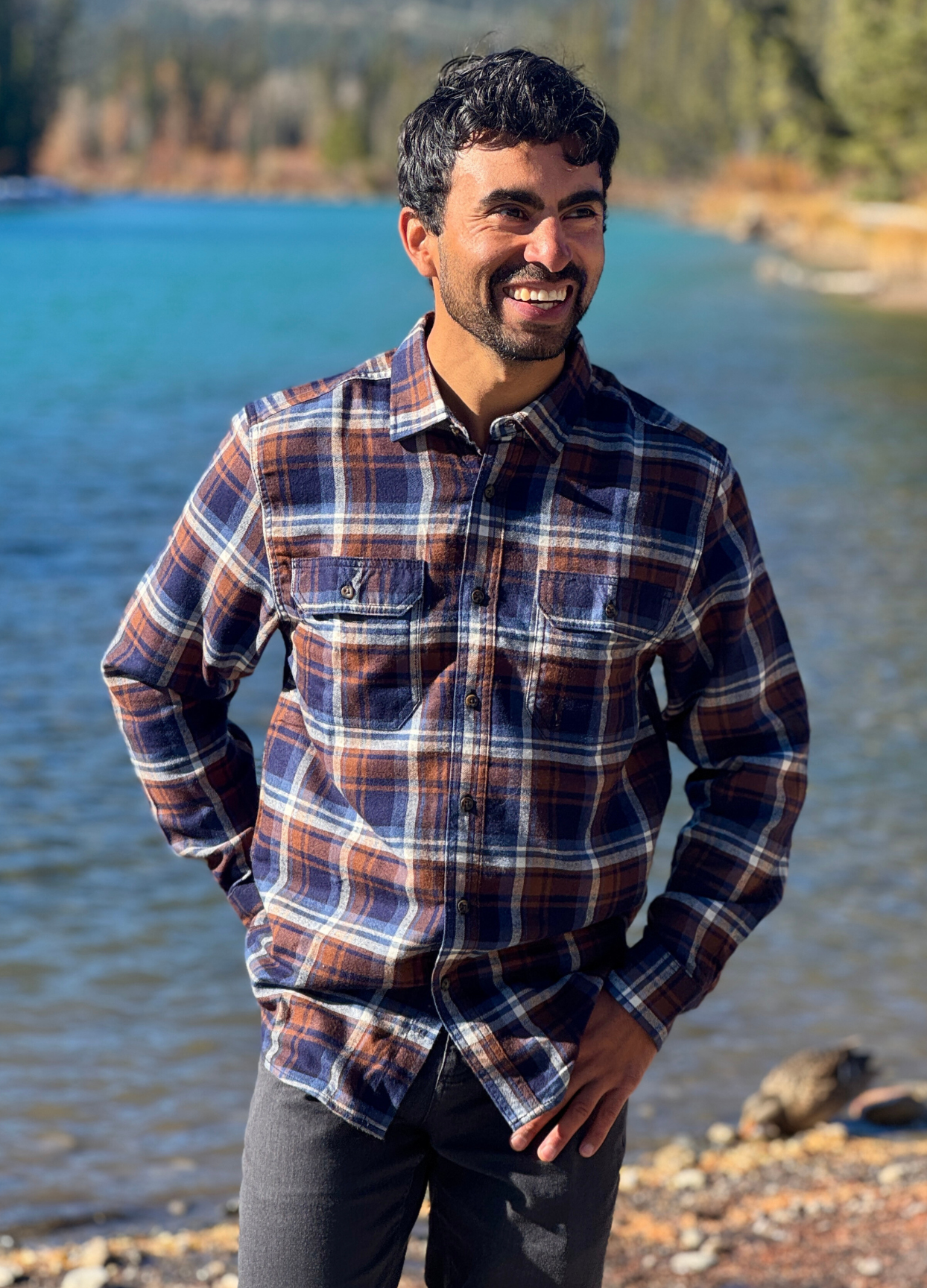 Man wearing a plaid flannel shirt standing by a river with trees in the background in Banff National Park