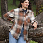 A girl standing outdoors wearing a plaid flannel jacket with a herringbone weave in a blend of brown and grey tones, buttoned at the cuffs and chest.