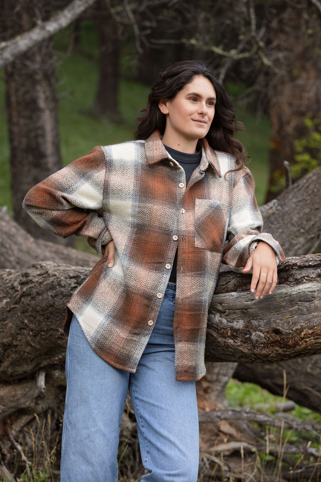 A girl standing outdoors wearing a plaid flannel jacket with a herringbone weave in a blend of brown and grey tones, buttoned at the cuffs and chest.