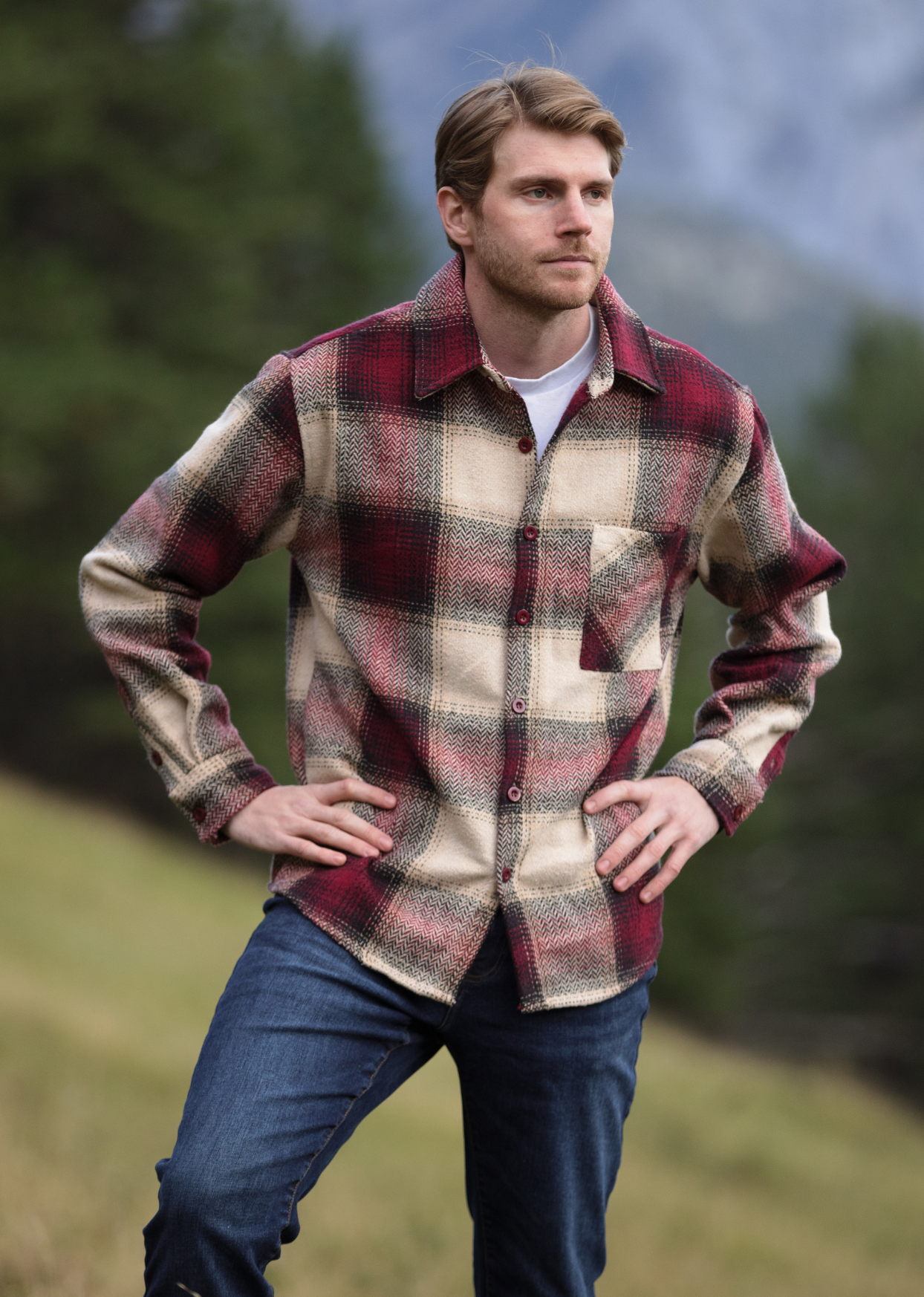 Man stood in field with hands on hip, modeling our burgundy wool jacket 