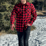 A man wearing a red and black buffalo check flannel shirt with two flap breast pockets and a button cuff, standing outdoors.