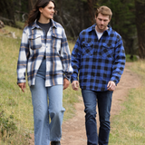 A man wearing a royal blue and black buffalo check padded flannel camping outdoor jacket with jeans.