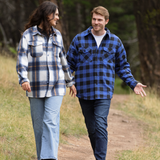 A man wearing a royal blue and black buffalo check padded flannel camping outdoor jacket with jeans.