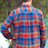 Back view of a man wearing a red and black buffalo check flannel shirt with two flap breast pockets and a button cuff, standing outdoors.
