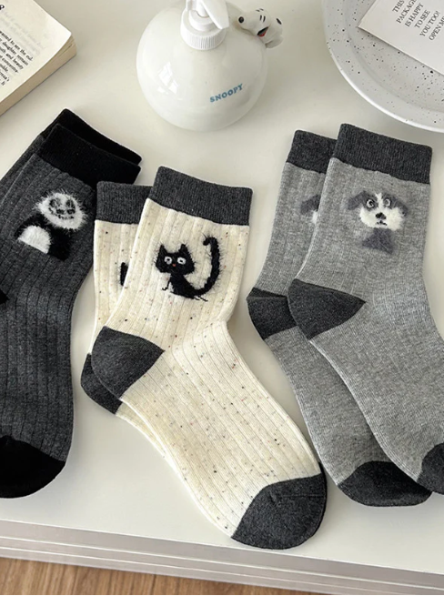 Four pairs of socks with animal designs on a surface with a book and small figurine.