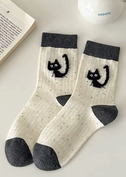 White socks with black cat designs and gray toes on a light surface.