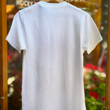 White t-shirt on a hanger with a blurred background of plants and text