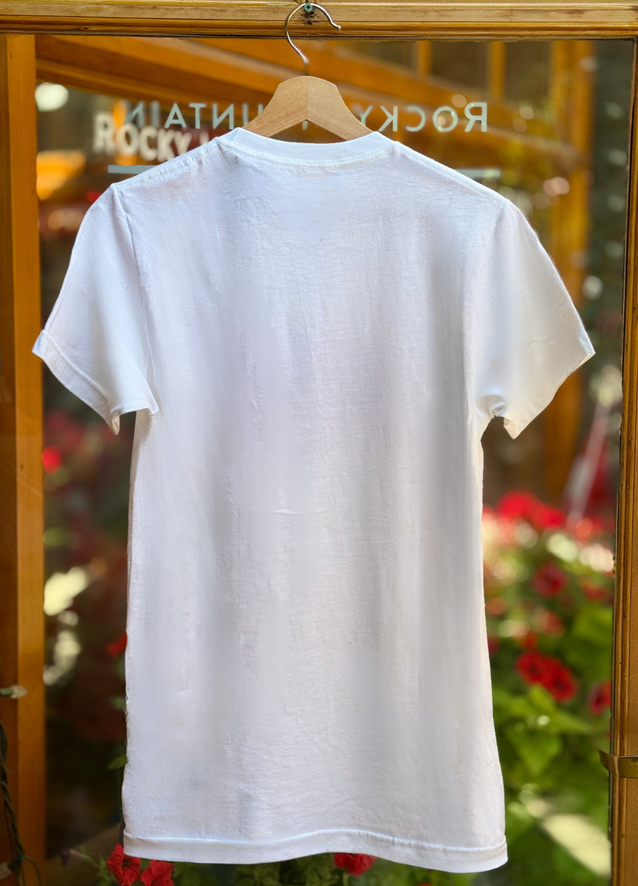 White t-shirt on a hanger with a blurred background of plants and text