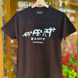 Black t-shirt with white graphic design and text 'Banff Canada' on a hanger against a blurred indoor background.