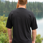 Man wearing a black t-shirt with a scenic background of trees and water