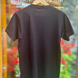 Black t-shirt on a hanger with a blurred background of flowers and a store entrance.