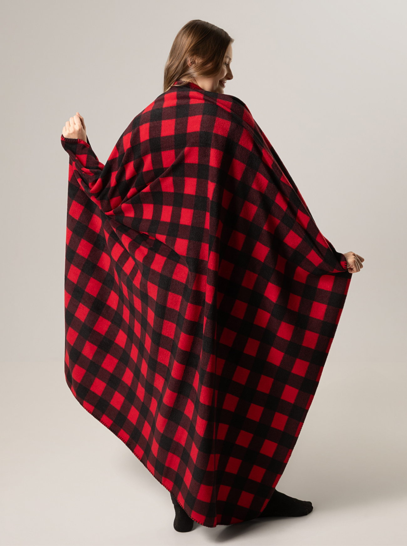 Person wearing a classic canadian red and black checkered blanket draped over them on a plain background