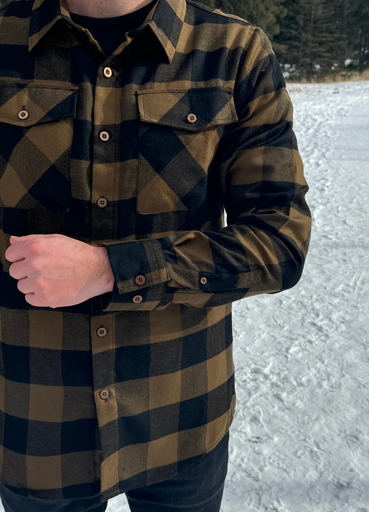 A man wearing a black and brown buffalo check flannel shirt with two flap breast pockets and two button cuff.