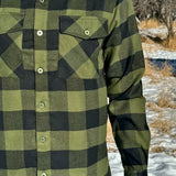 A man wearing a black and olive buffalo check flannel shirt with two flap breast pockets and a two button cuff.