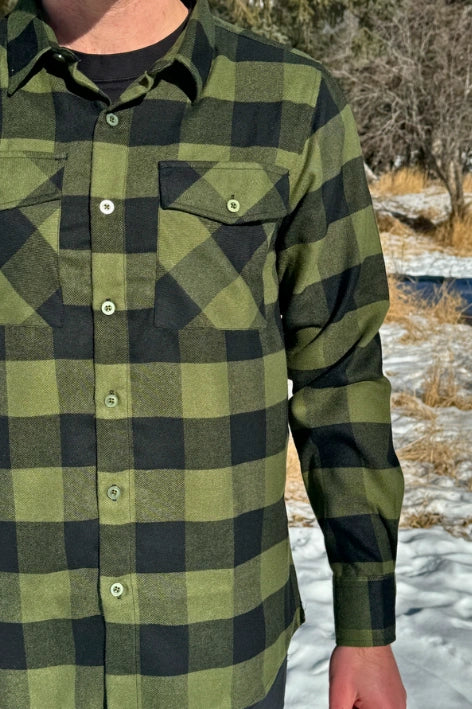 A man wearing a black and olive buffalo check flannel shirt with two flap breast pockets and a two button cuff.