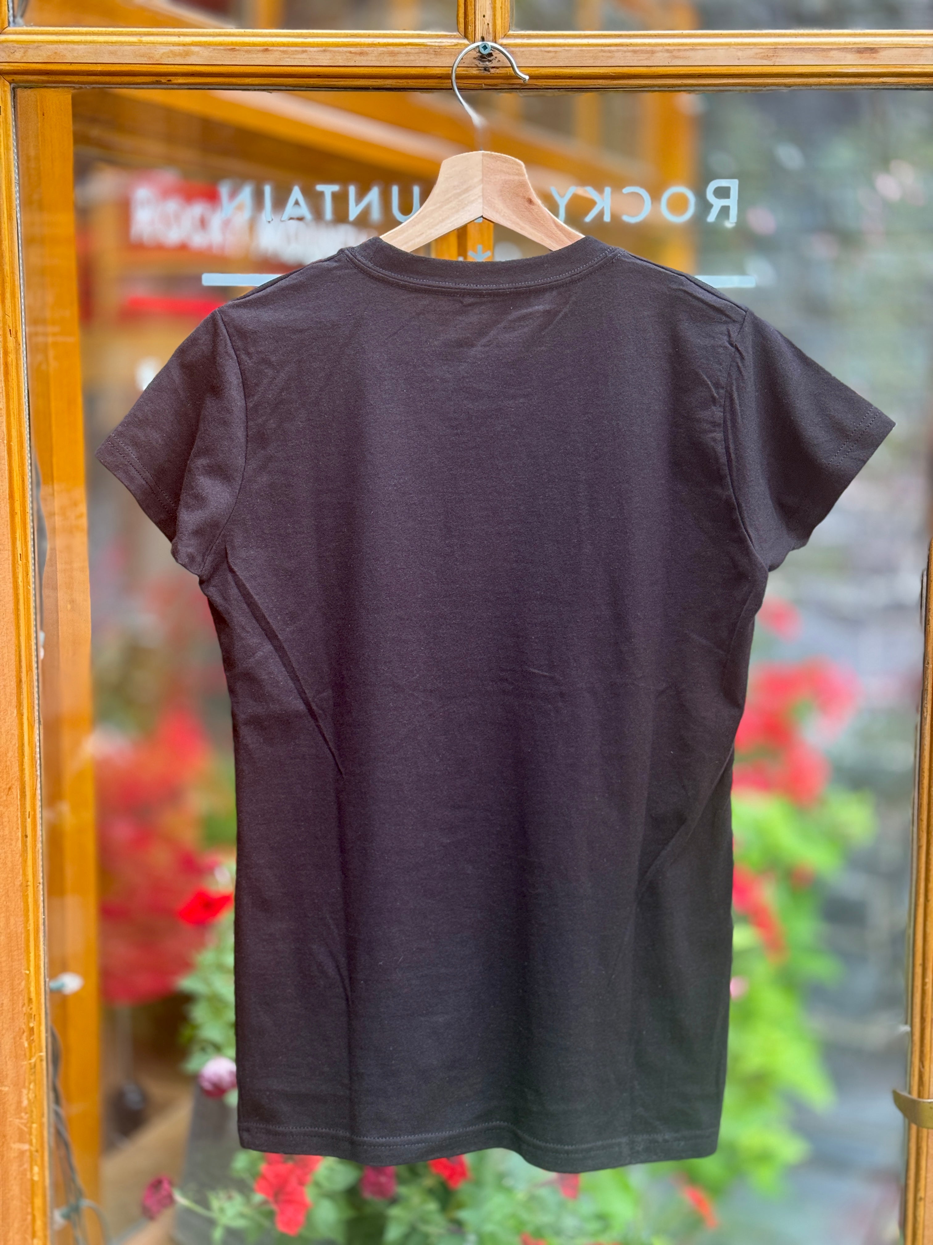 Black t-shirt on a hanger with a blurred background of flowers and store signs.